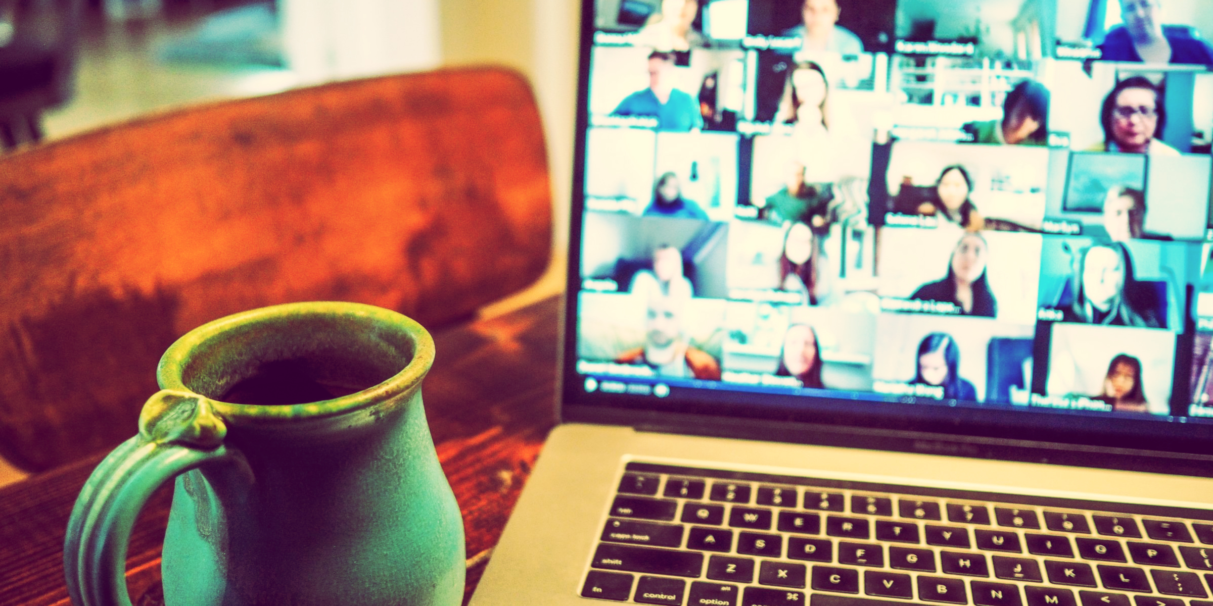 A laptop and a mug of coffee, on the screen of the laptop are several people on a zoom call.